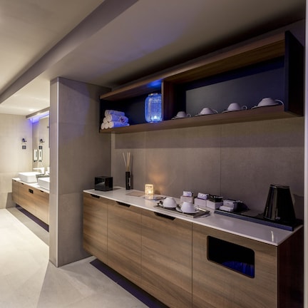 A modern hotel bathroom with a large mirror, wooden vanity, and a shelf with toiletries.