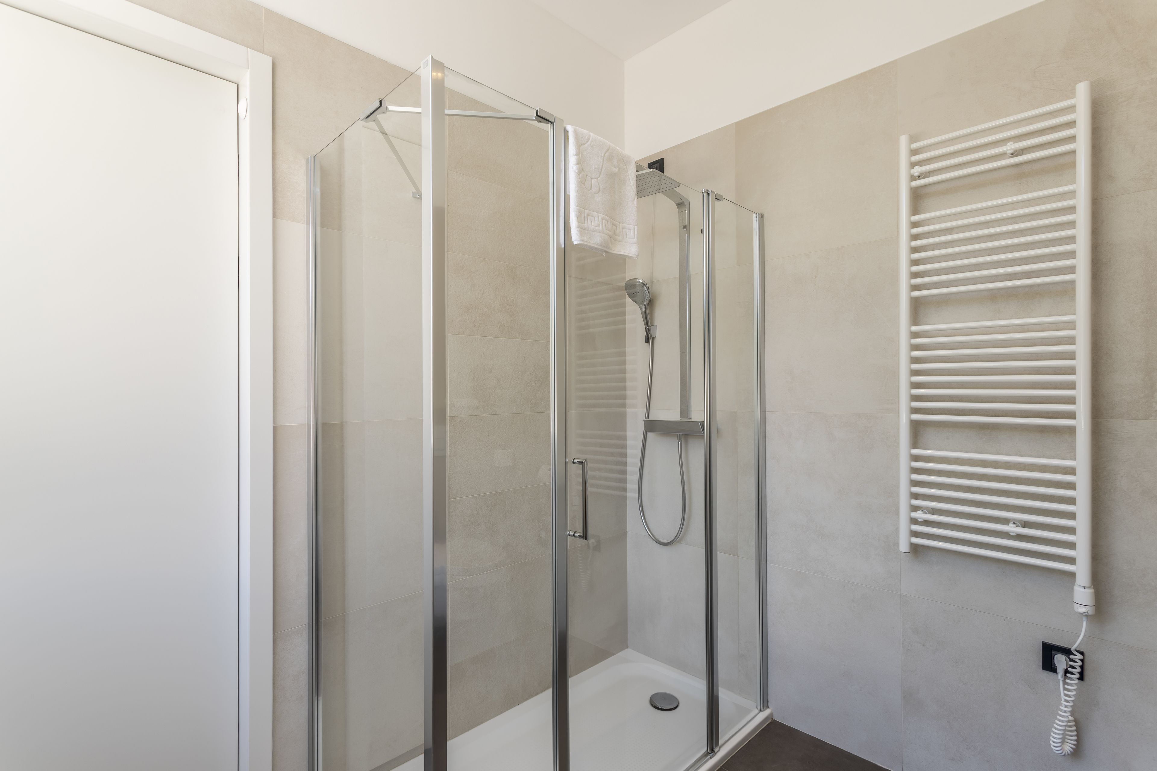 A modern bathroom with a glass-enclosed shower, a white towel hanging on the wall, and a built-in towel rack.