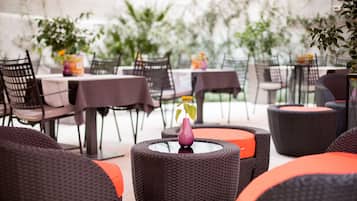 An outdoor dining area with wicker chairs and tables, some with orange cushions.