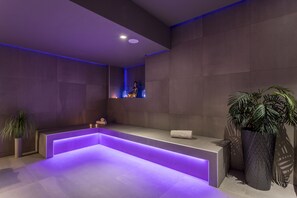 A modern bathroom with a built-in bathtub, a bench, and a potted plant.