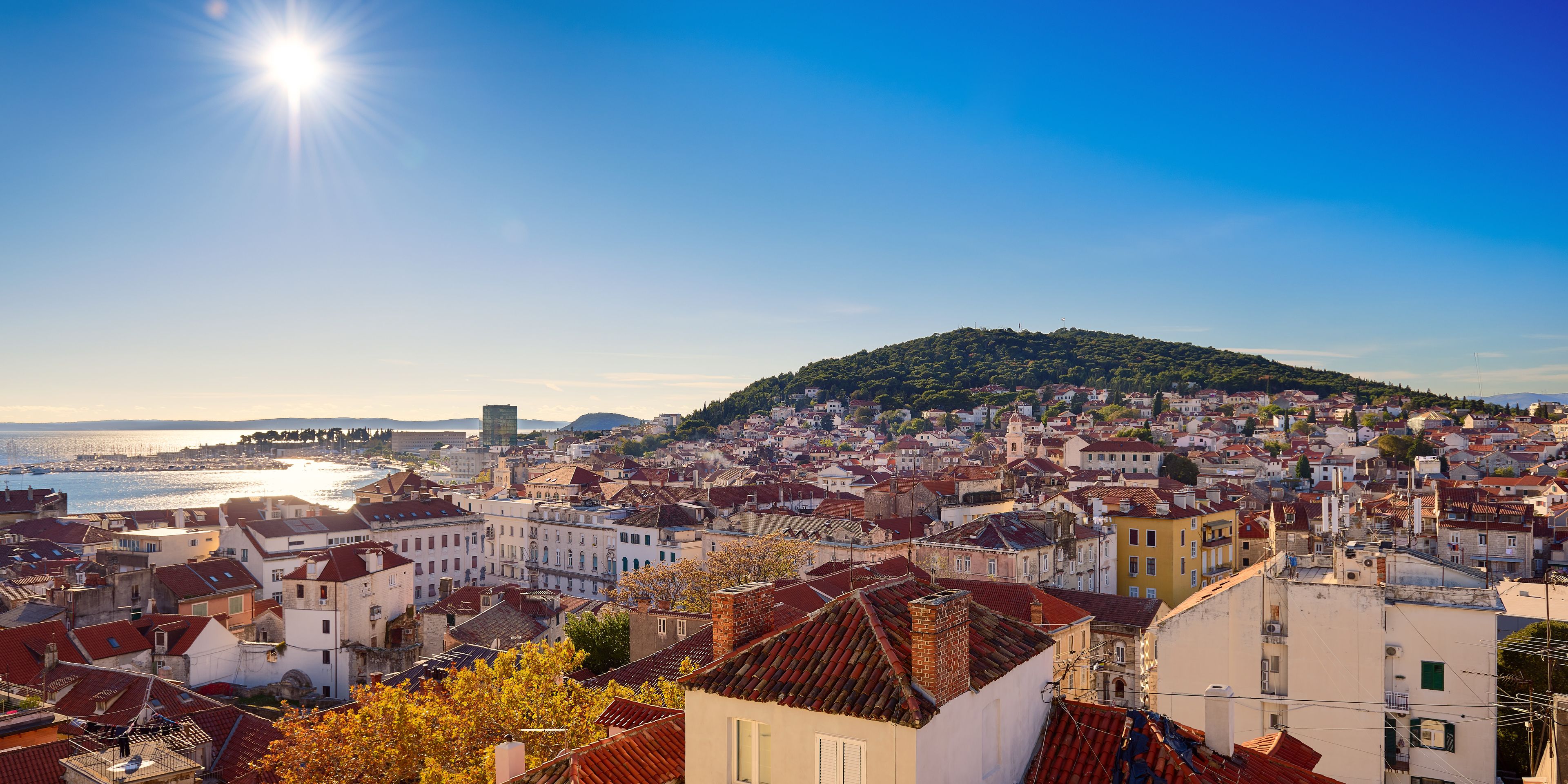 A coastal cityscape with historic buildings, a hilltop, and a view of the sea.