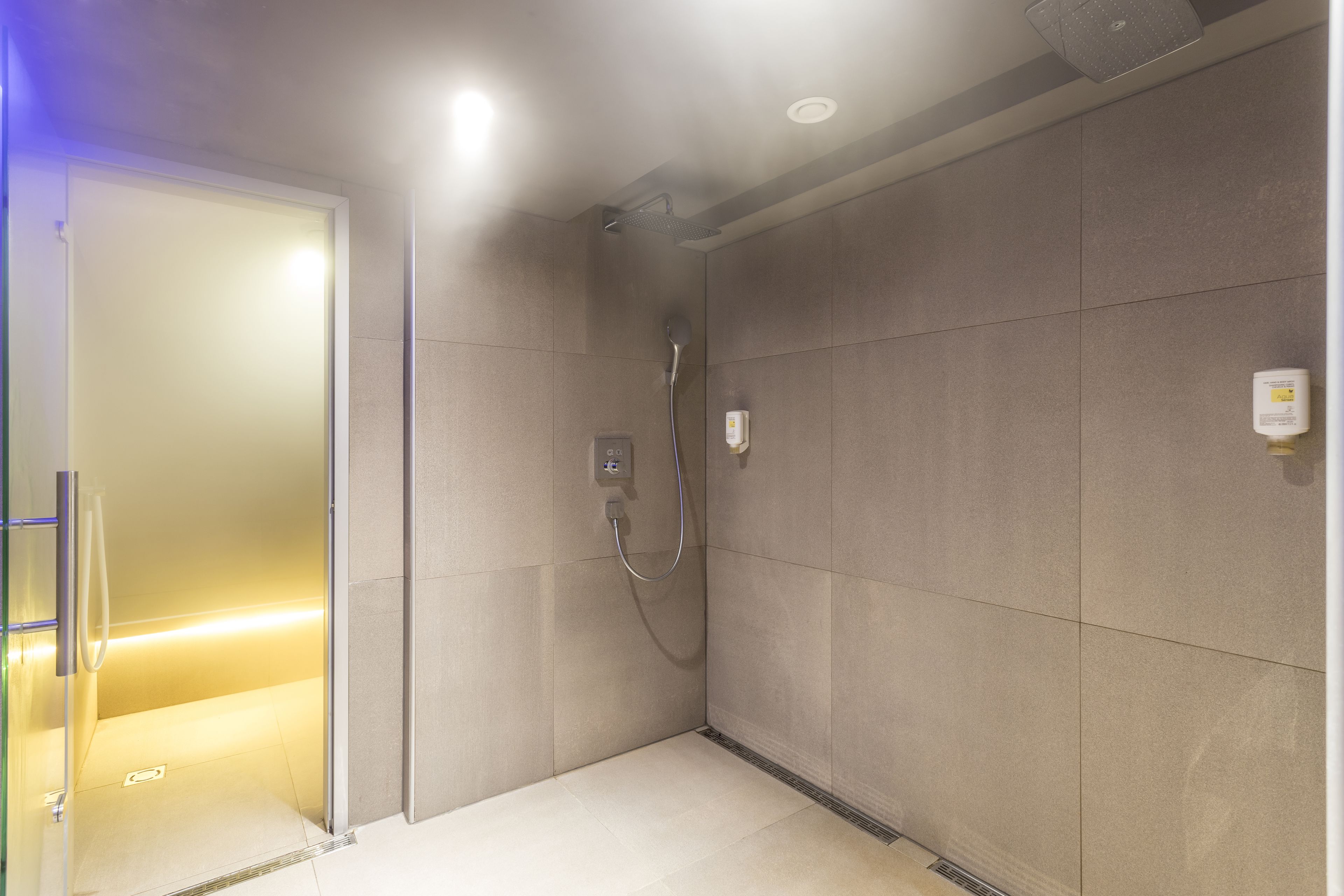 Un espace douche moderne doté d’une porte en verre, d’un pommeau de douche à main et d’un panneau de commande fixé au mur.