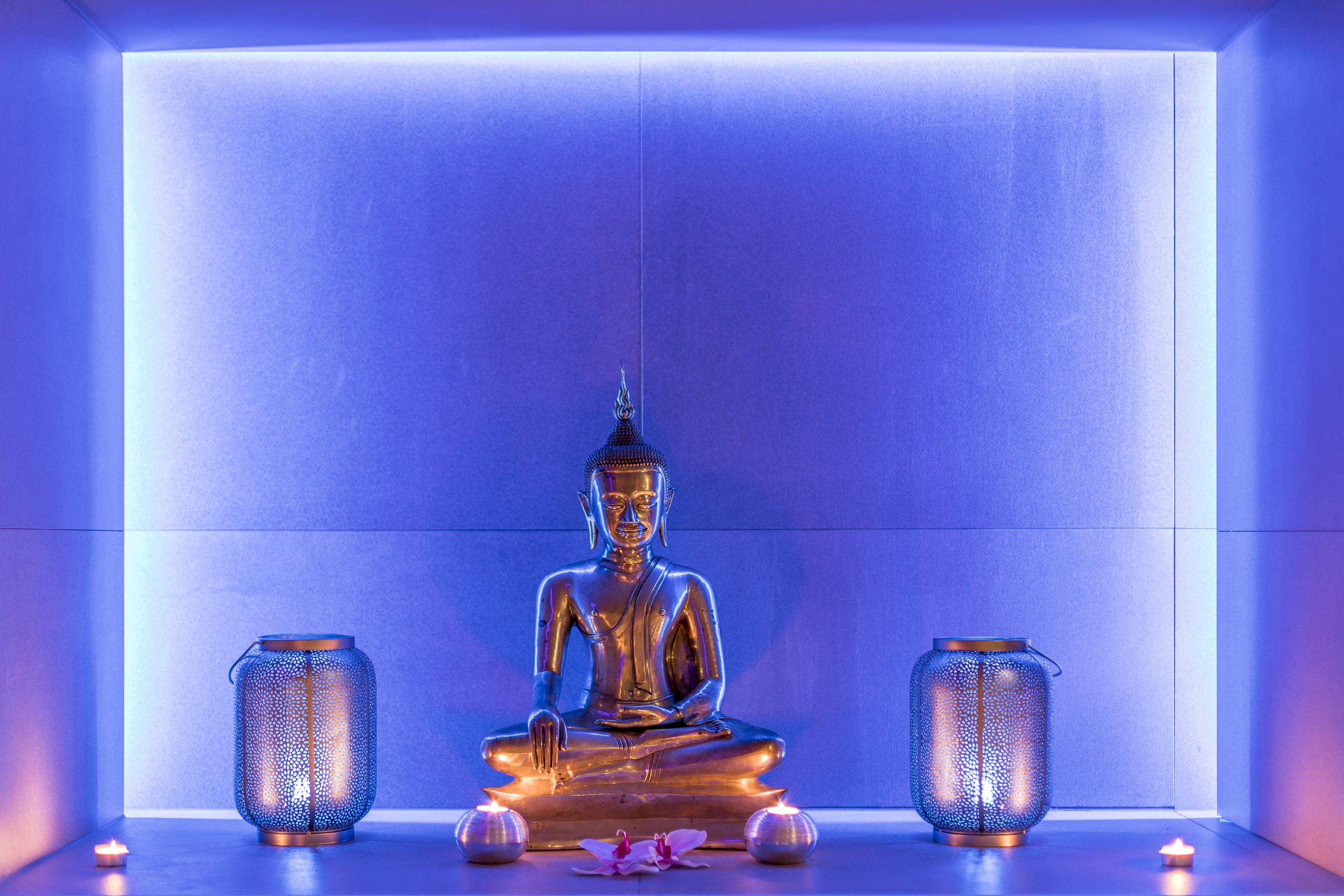 A statue of Buddha in a meditative pose, flanked by two lanterns on a reflective surface.