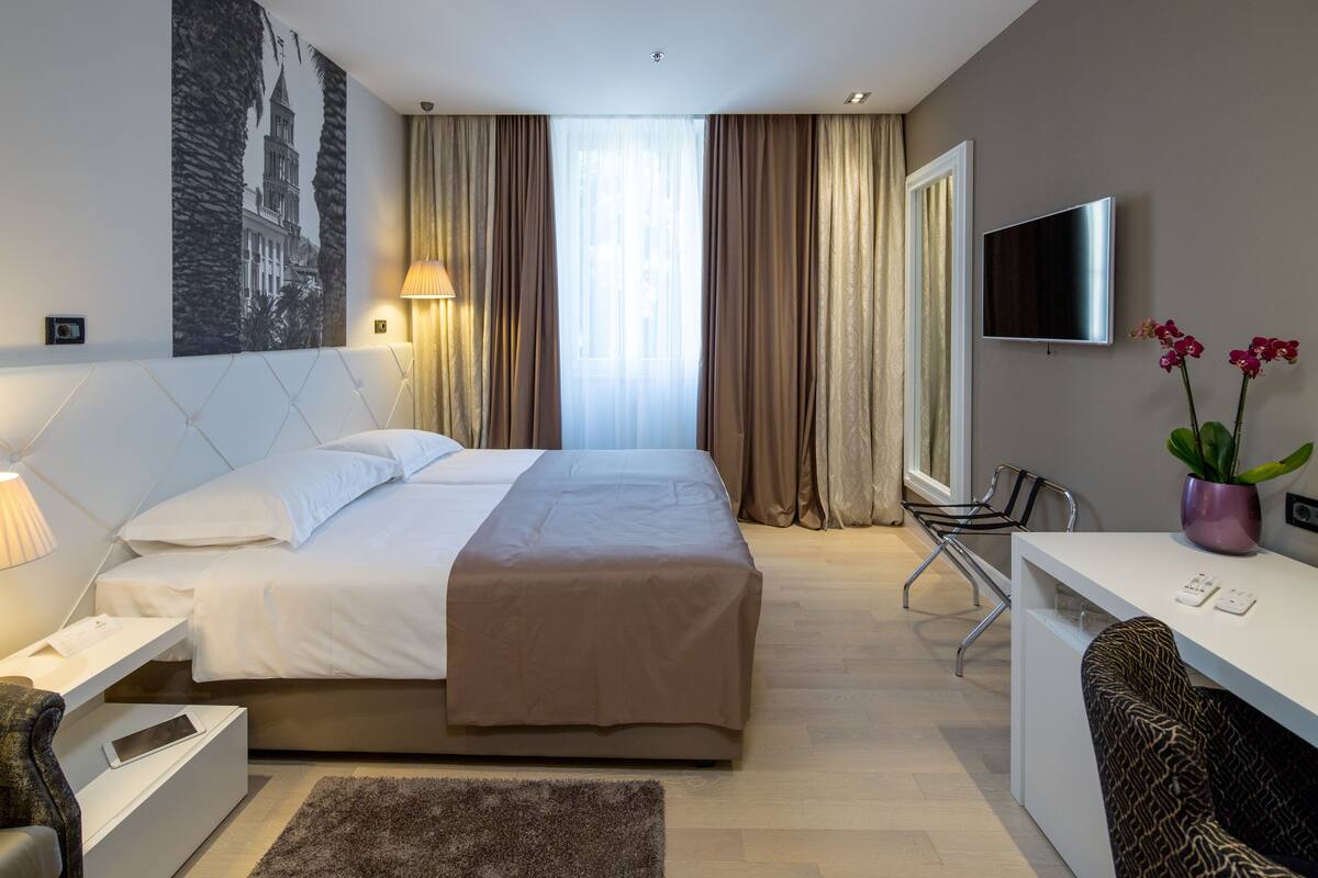A hotel room with a bed, a desk, a chair, a TV, and a window with curtains.