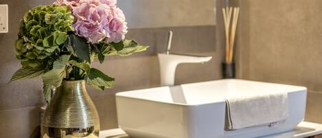 A bathroom vanity with a white sink, a vase with flowers, and a mirror above the vanity.