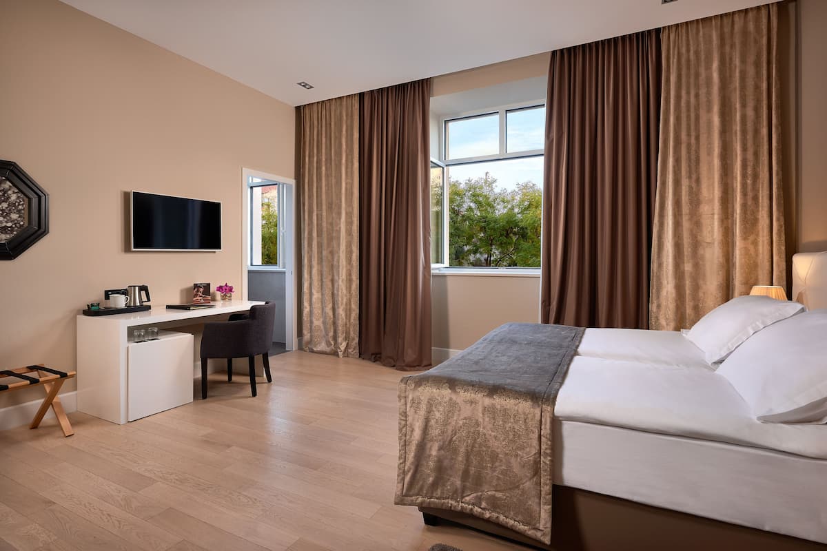 A hotel room with a bed, desk, chair, TV, and large windows.