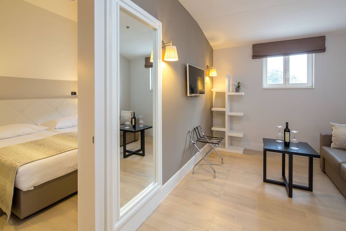 A modern bedroom with a bed, a small table with a bottle and glasses, a chair, and a TV on the wall.