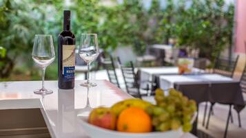 Una mesa con una botella de vino, dos copas y un cuenco de fruta en un entorno al aire libre.
