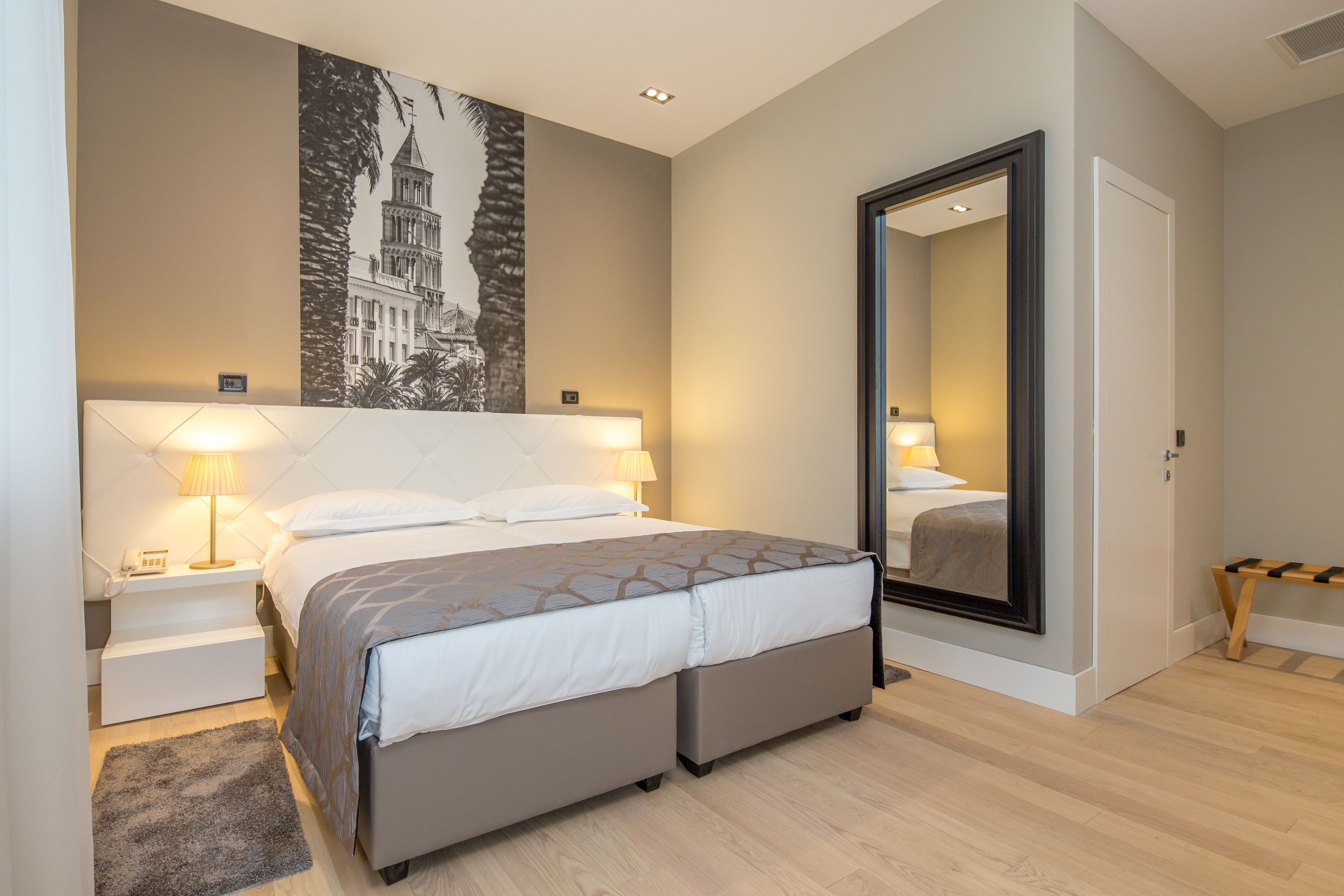Un hotel moderno con una cama grande, lámparas de noche, un espejo y un cuadro en la pared.