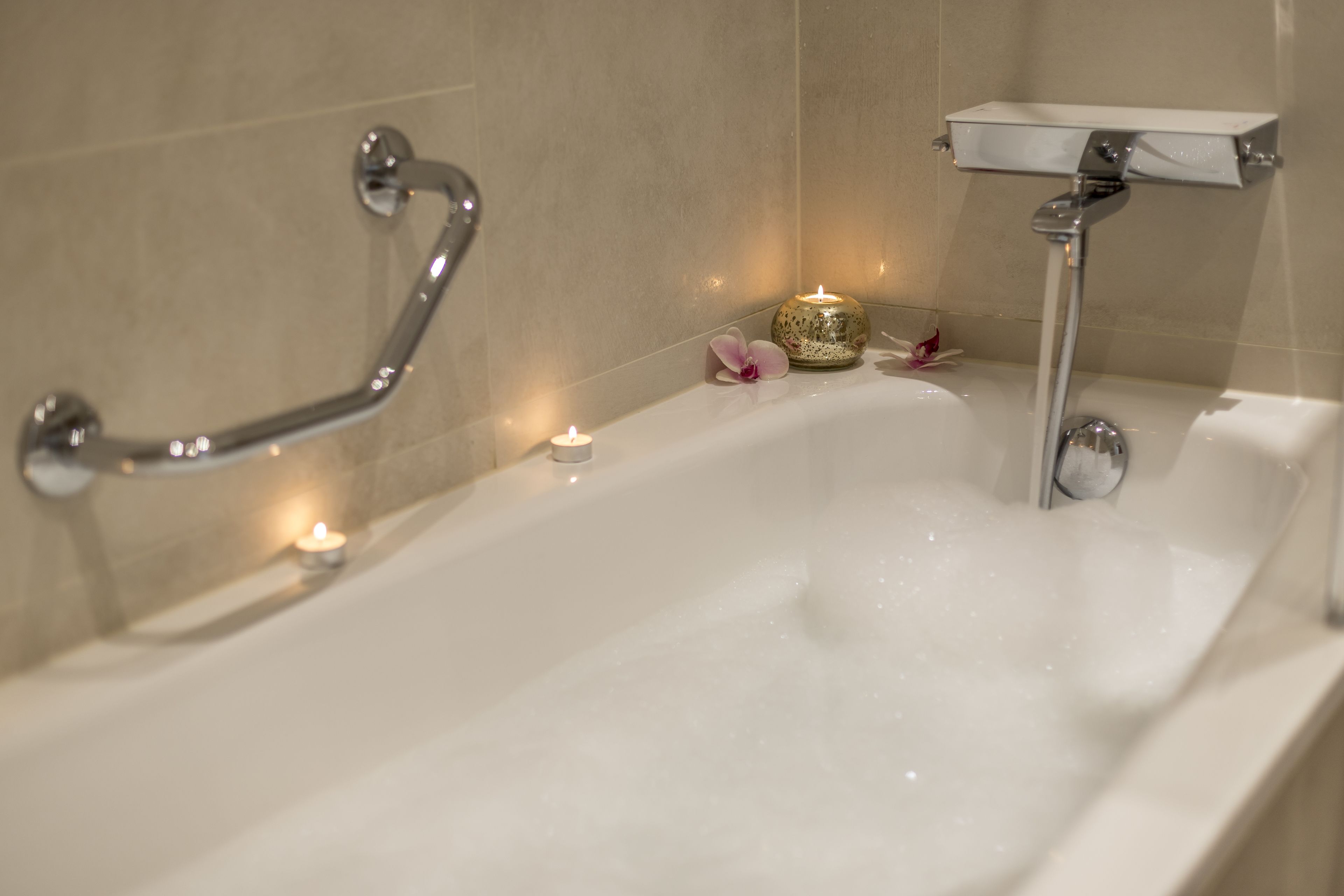 Une baignoire avec un pommeau de douche amovible, un récipient en verre et des bougies.