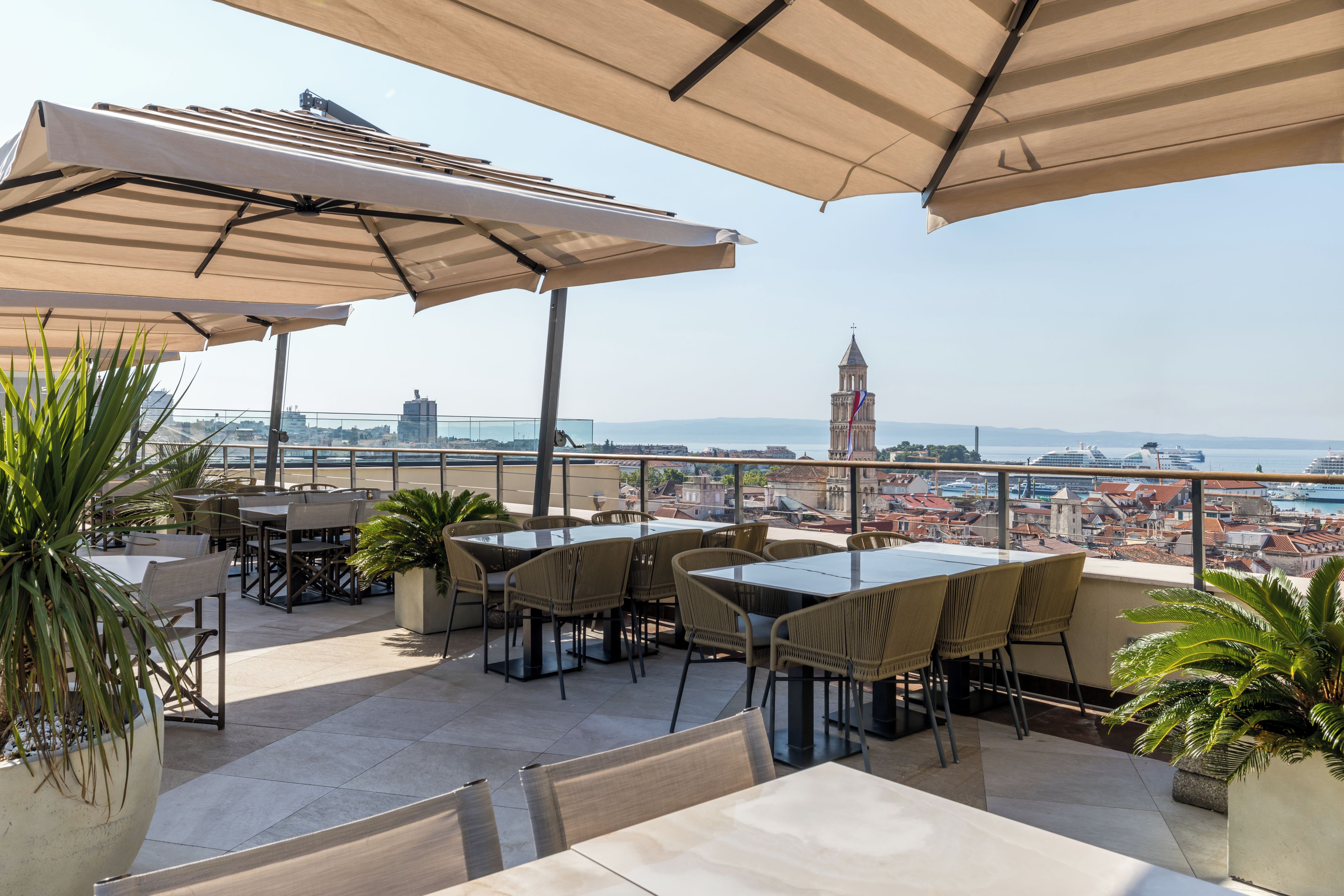 An outdoor terrace with tables and chairs, umbrellas, and potted plants.