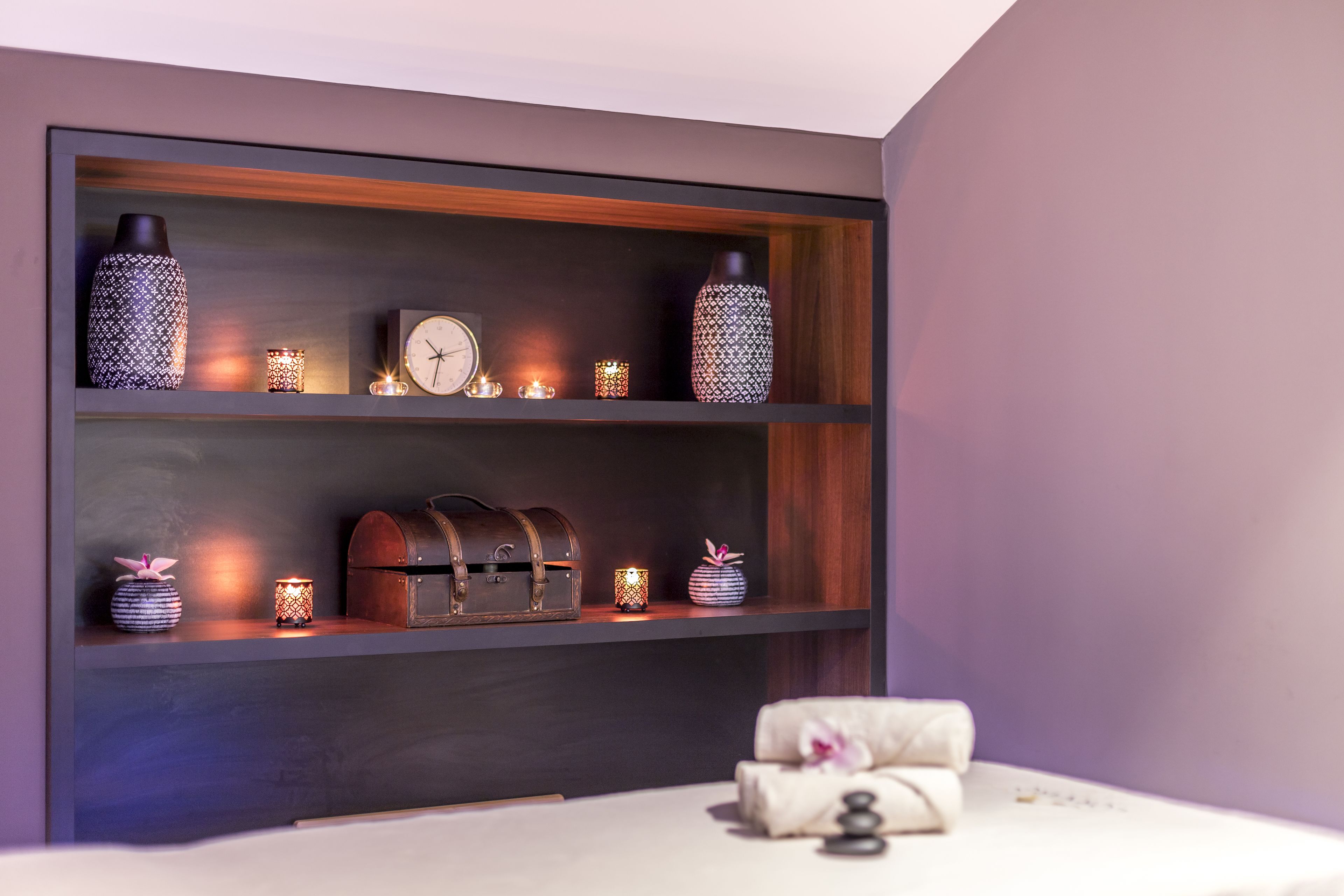 A bedroom with a bed, a shelf with decorative items, and a clock.