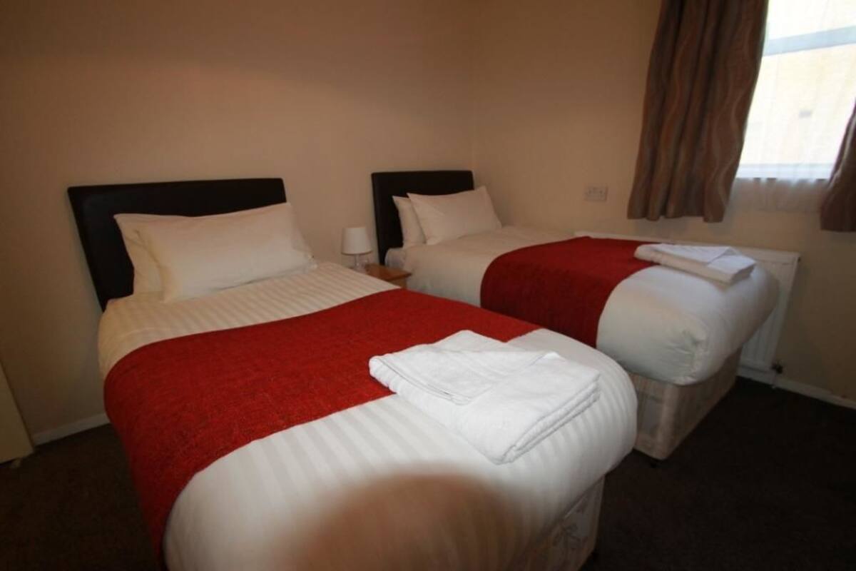 A hotel room with two beds, each with a red blanket and white pillows.