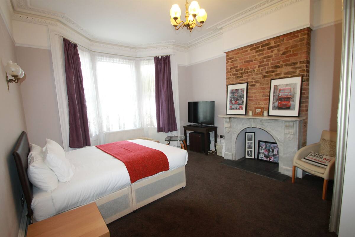 A bedroom with a bed, a television, a fireplace, and a brick wall.