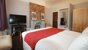 A hotel room with a large bed, a television, a fireplace, and a mirror.