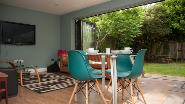 A modern dining area with teal chairs, a glass table, and a view of the garden through large windows.