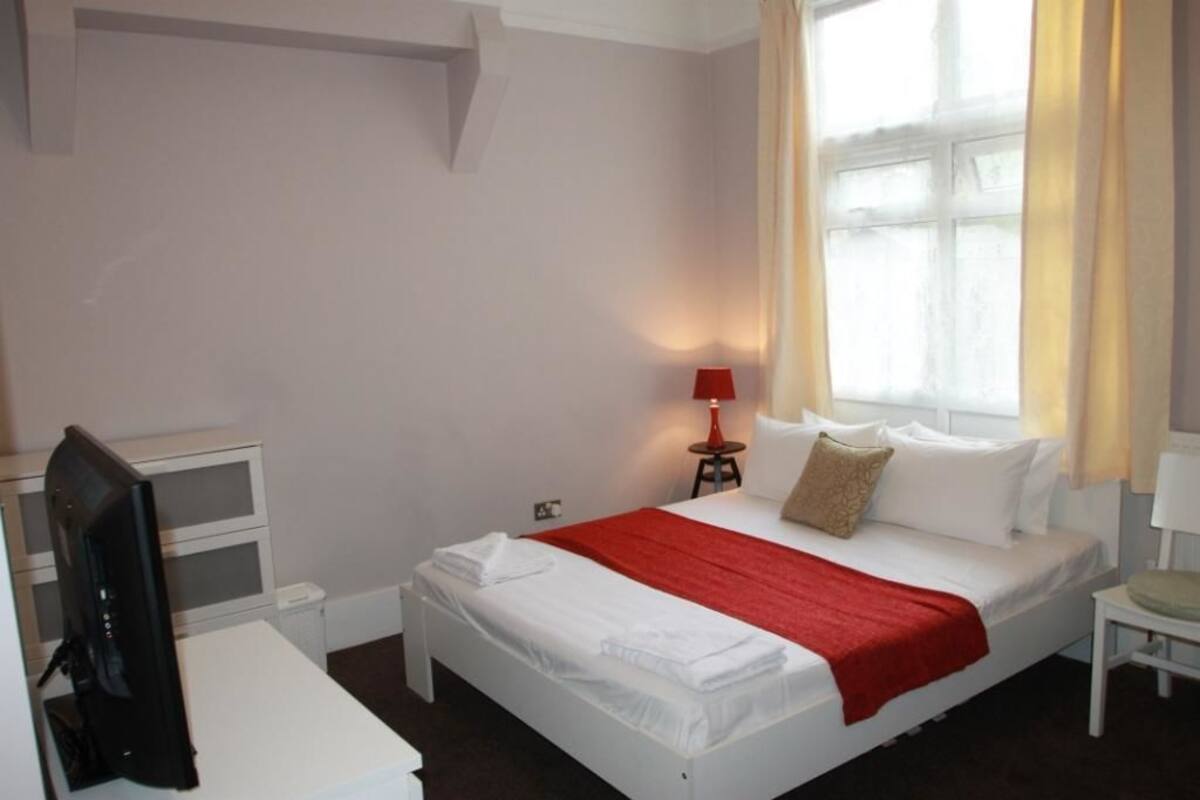 A hotel room with a bed, a desk, a chair, a TV, and a window with curtains.