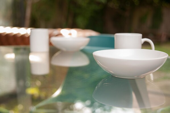 Une table avec des bols et des tasses en céramique blanche, une bougie et une table en verre qui reflète l’environnement.