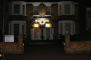 The exterior of Manor House Hotel with a classic architectural style, featuring a prominent entrance with two illuminated windows and a sign above the door. - Manor House London (London)