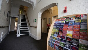 A hotel hallway with a staircase, a wall of travel brochures, and a framed picture on the wall.
