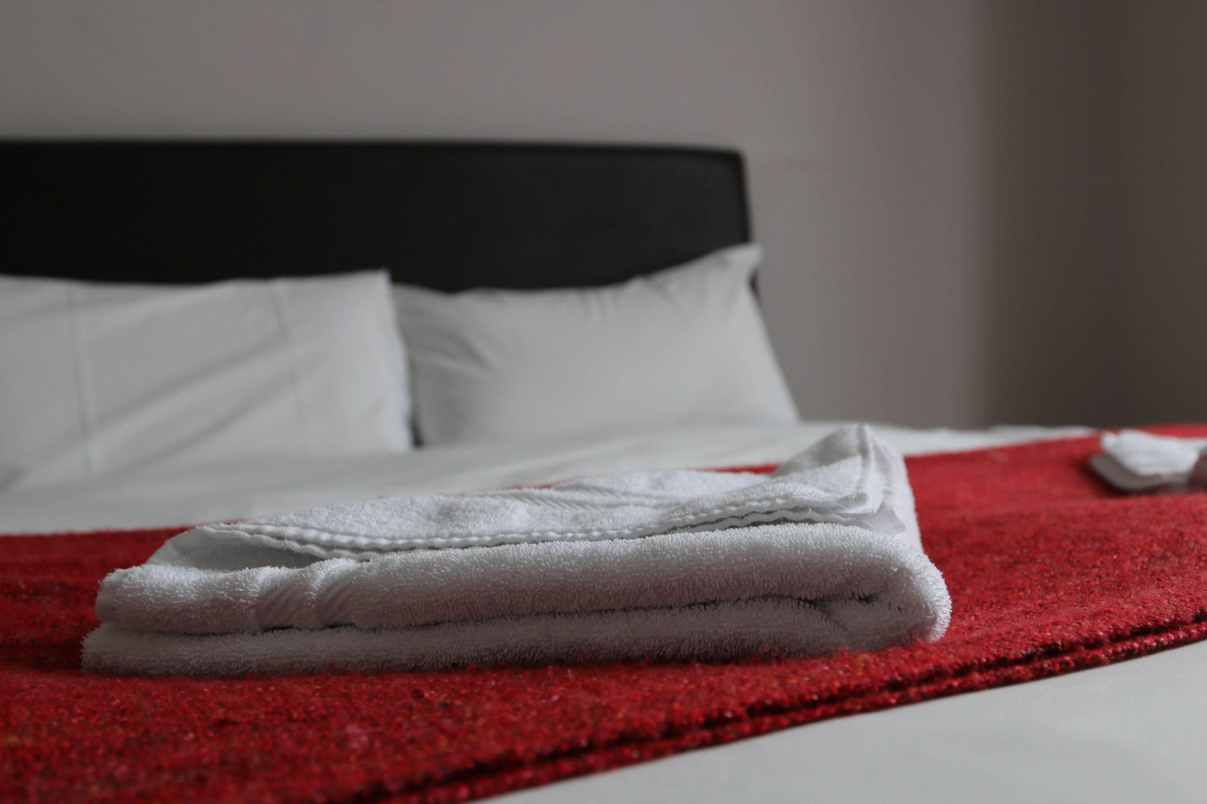 A neatly made bed with white linens and a red blanket, a black headboard, and white pillows.