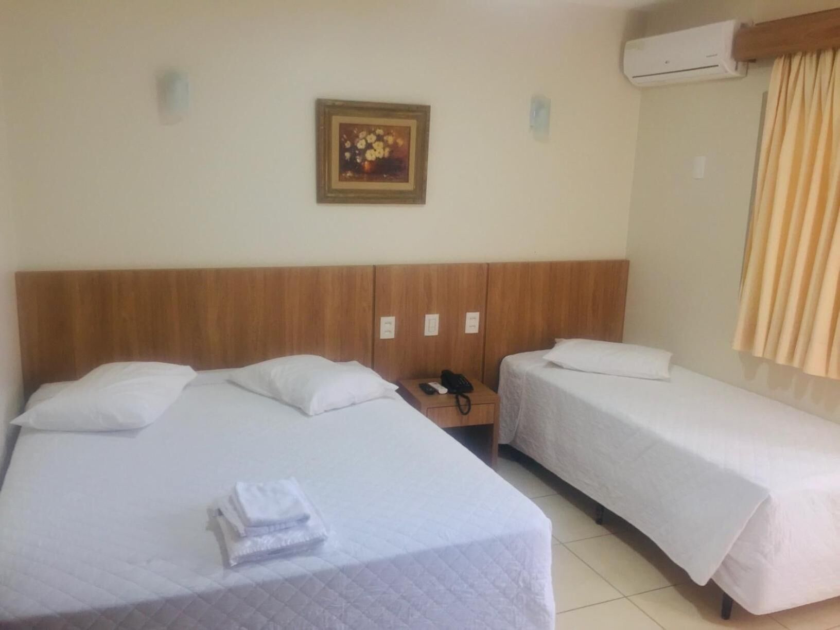 Habitación de hotel con dos camas, cabecero de madera, mesita de noche con teléfono y aire acondicionado instalado en la pared.