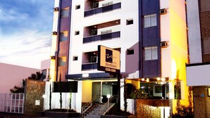 A modern hotel with a signboard, multiple balconies, and a well-lit entrance.