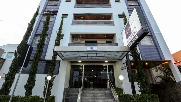 A modern hotel entrance with a glass facade, a staircase leading to the entrance, and a sign indicating the hotel name.