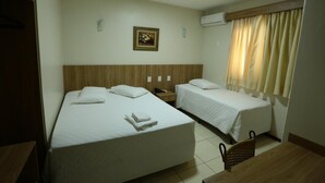 A hotel room with two beds, a wooden headboard, a small table, a chair, a picture on the wall, and a window with curtains.