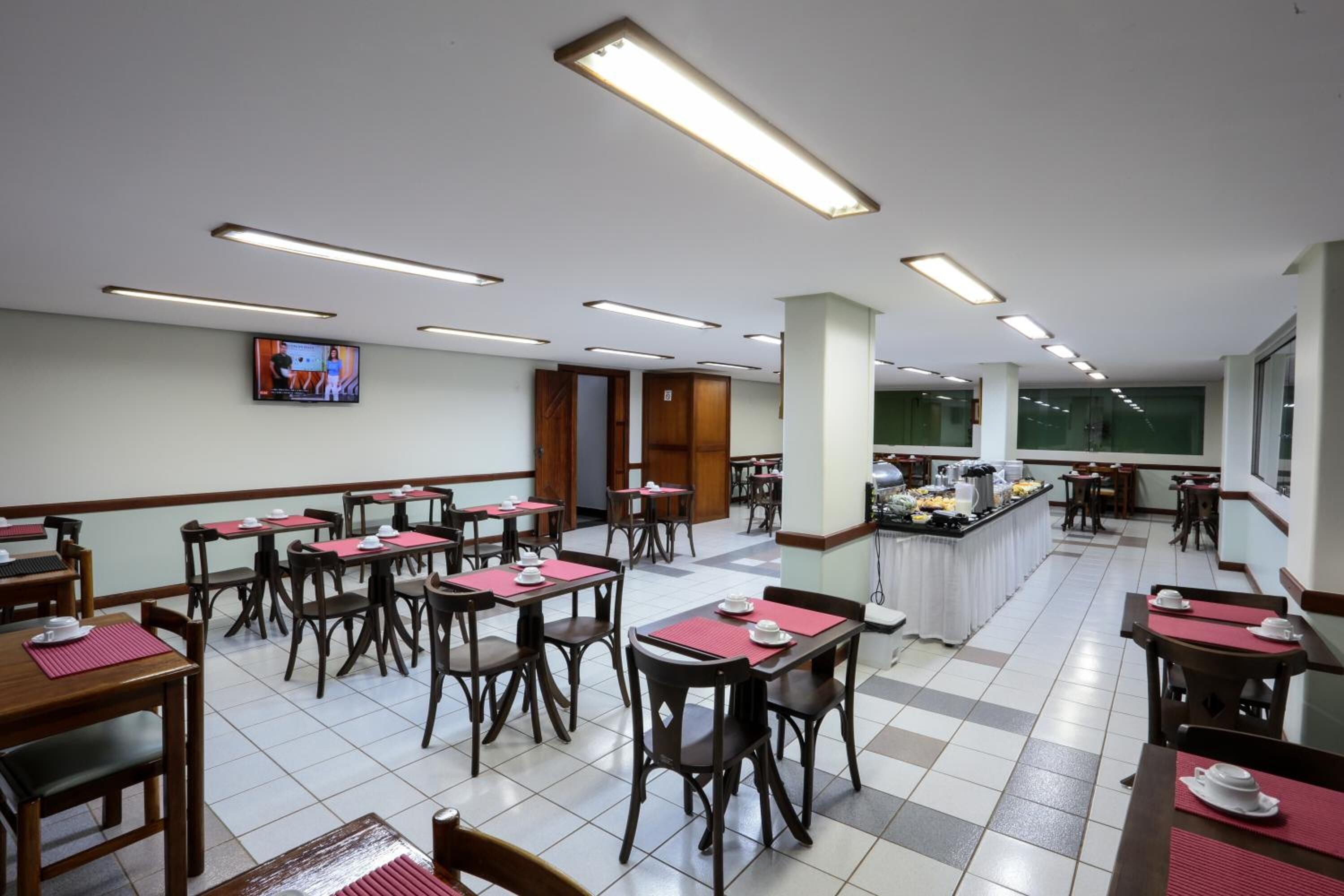 A spacious dining area with multiple tables and chairs, a buffet counter, and a television mounted on the wall.