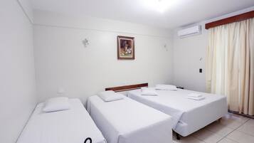 Habitación de hotel con tres camas individuales, un cabecero de madera, un aire acondicionado de pared y un cuadro enmarcado sobre las camas.