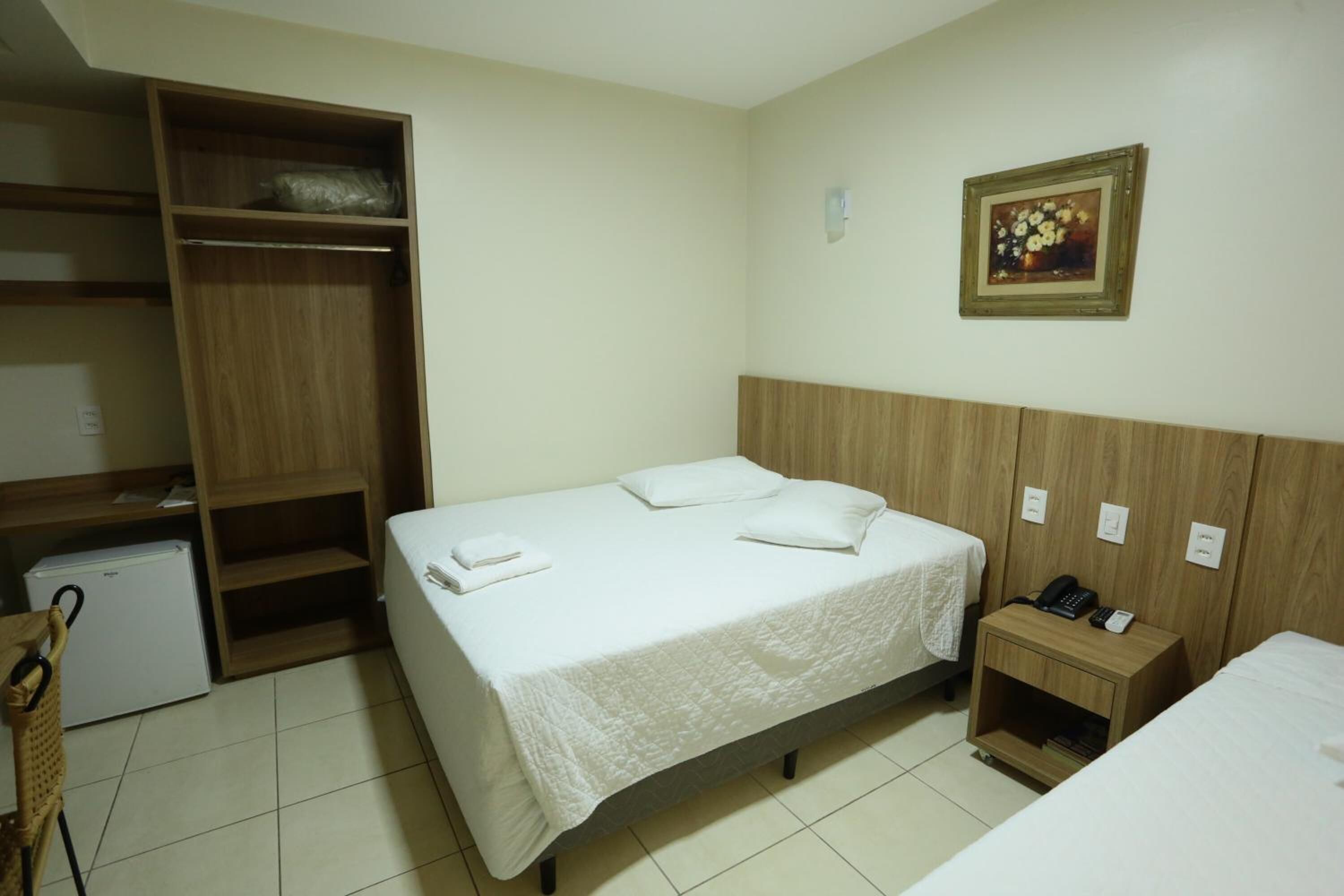 A hotel room with a bed, a wardrobe, a small table with a phone, and a picture on the wall.