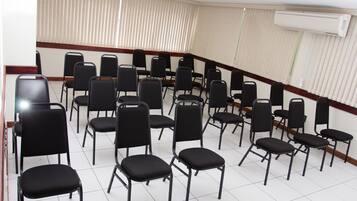 Un salón de conferencias con filas de sillas negras, una barandilla de madera y un equipo de aire acondicionado en la pared.