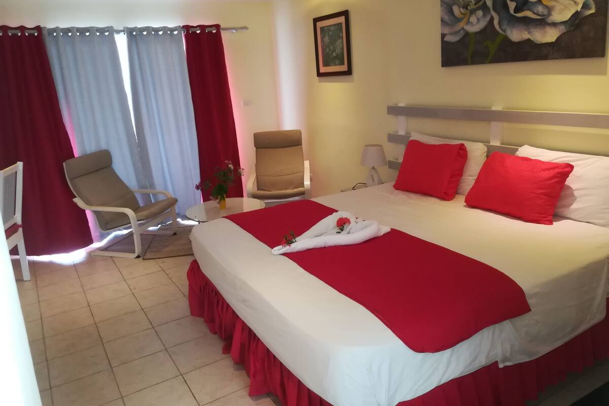 Hotellihuone, jossa on sänky, kaksi tuolia, työpöytä ja taulu seinällä.