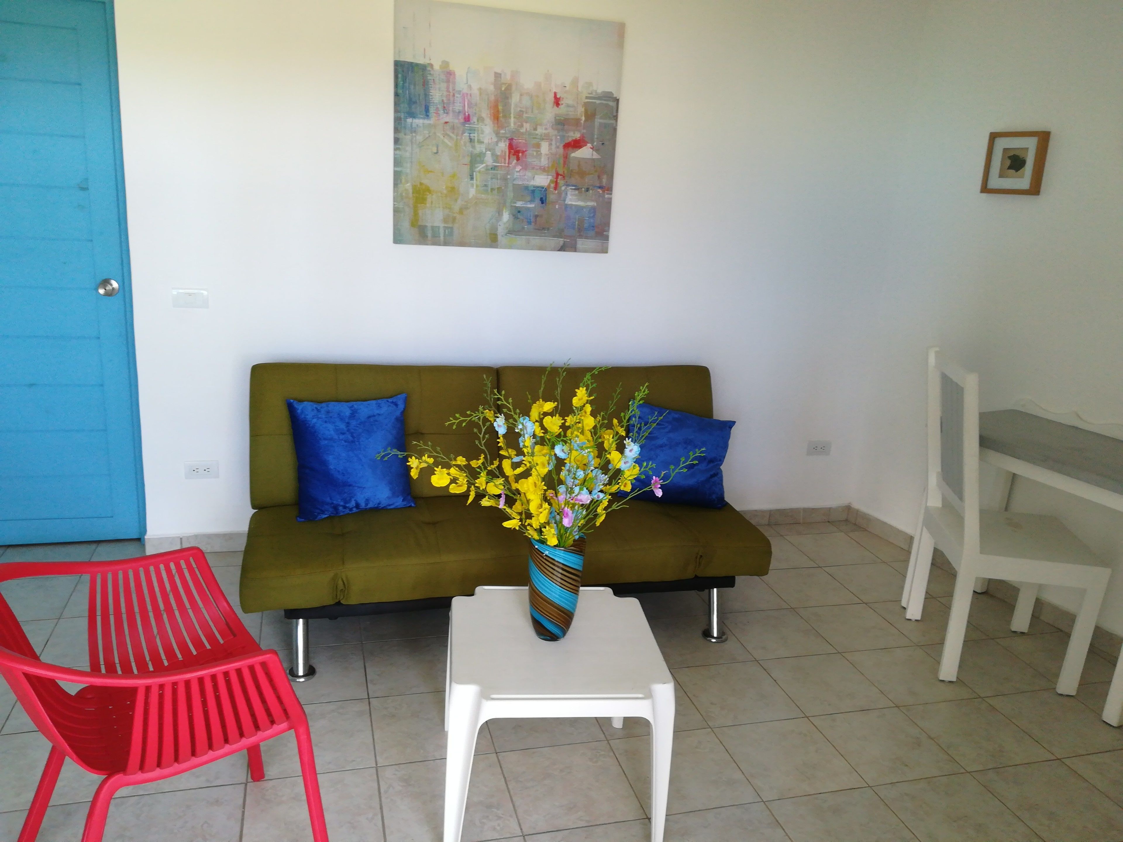 A living room with a green sofa, two blue pillows, a white coffee table, and a red chair.
