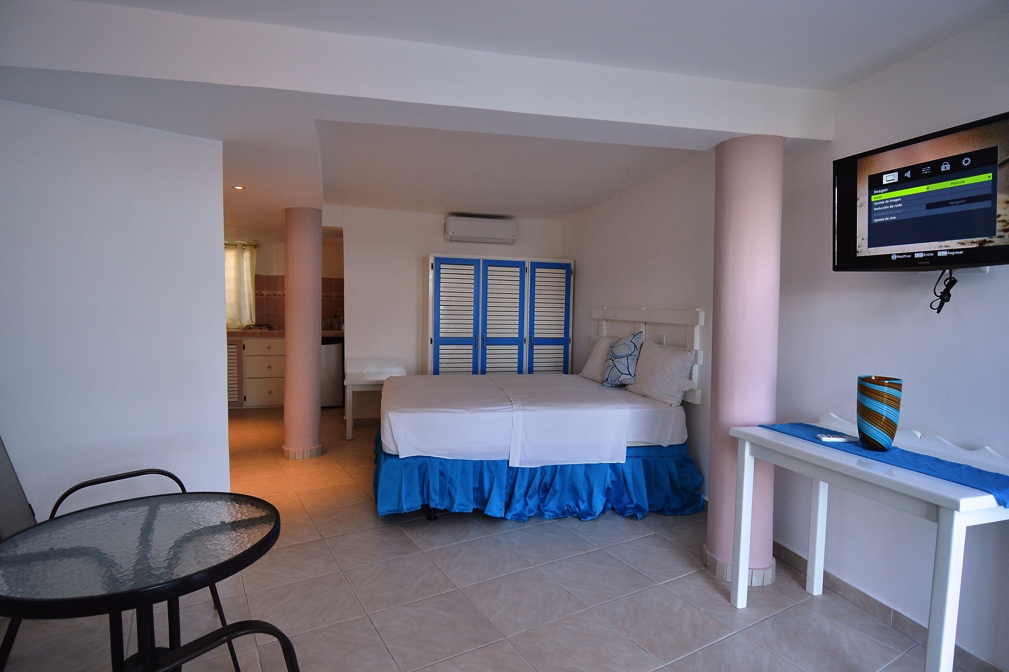 A hotel room with a bed, a TV mounted on the wall, a desk with a vase, and a chair.