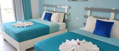Dos camas individuales con ropa de cama color turquesa y cabeceros blancos, un cuadro en la pared y una ventana con cortinas.