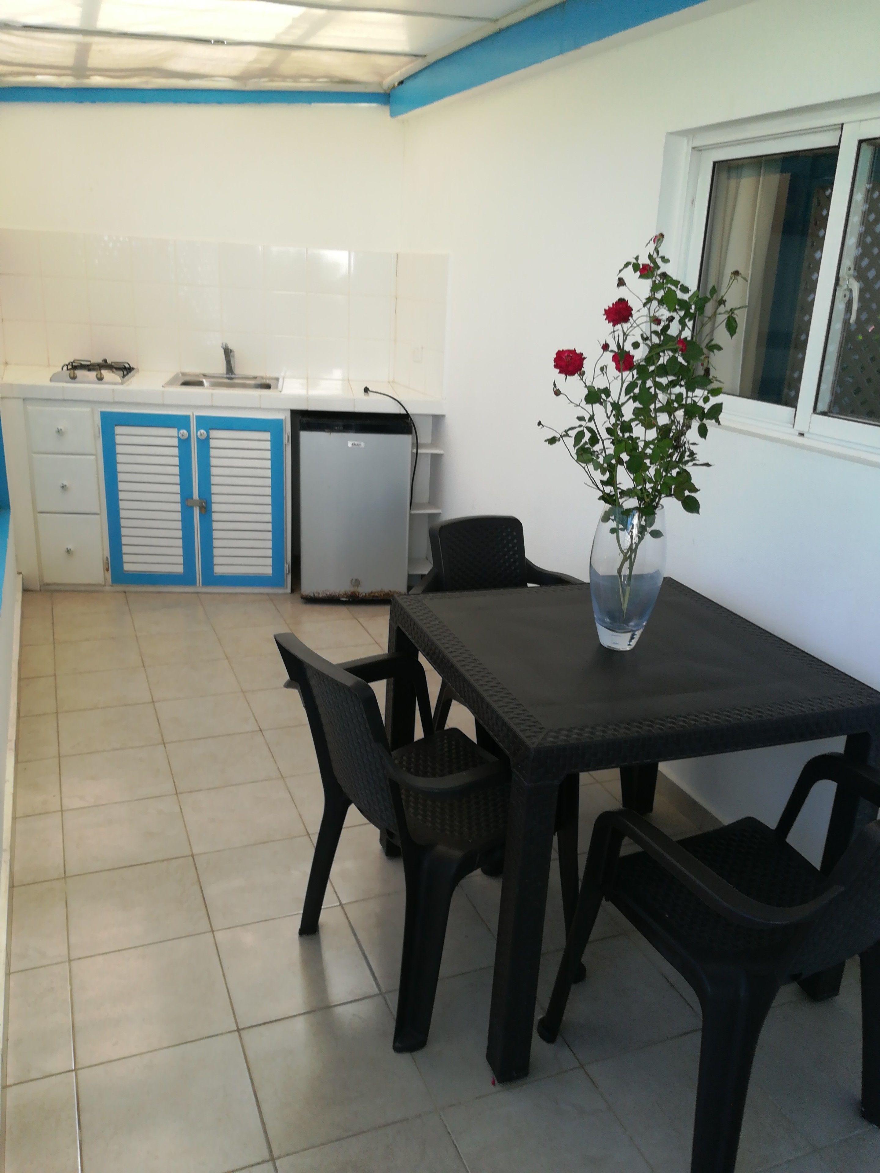 A kitchen with white cabinets and blue handles, a small refrigerator, and a dining area with a table and chairs.