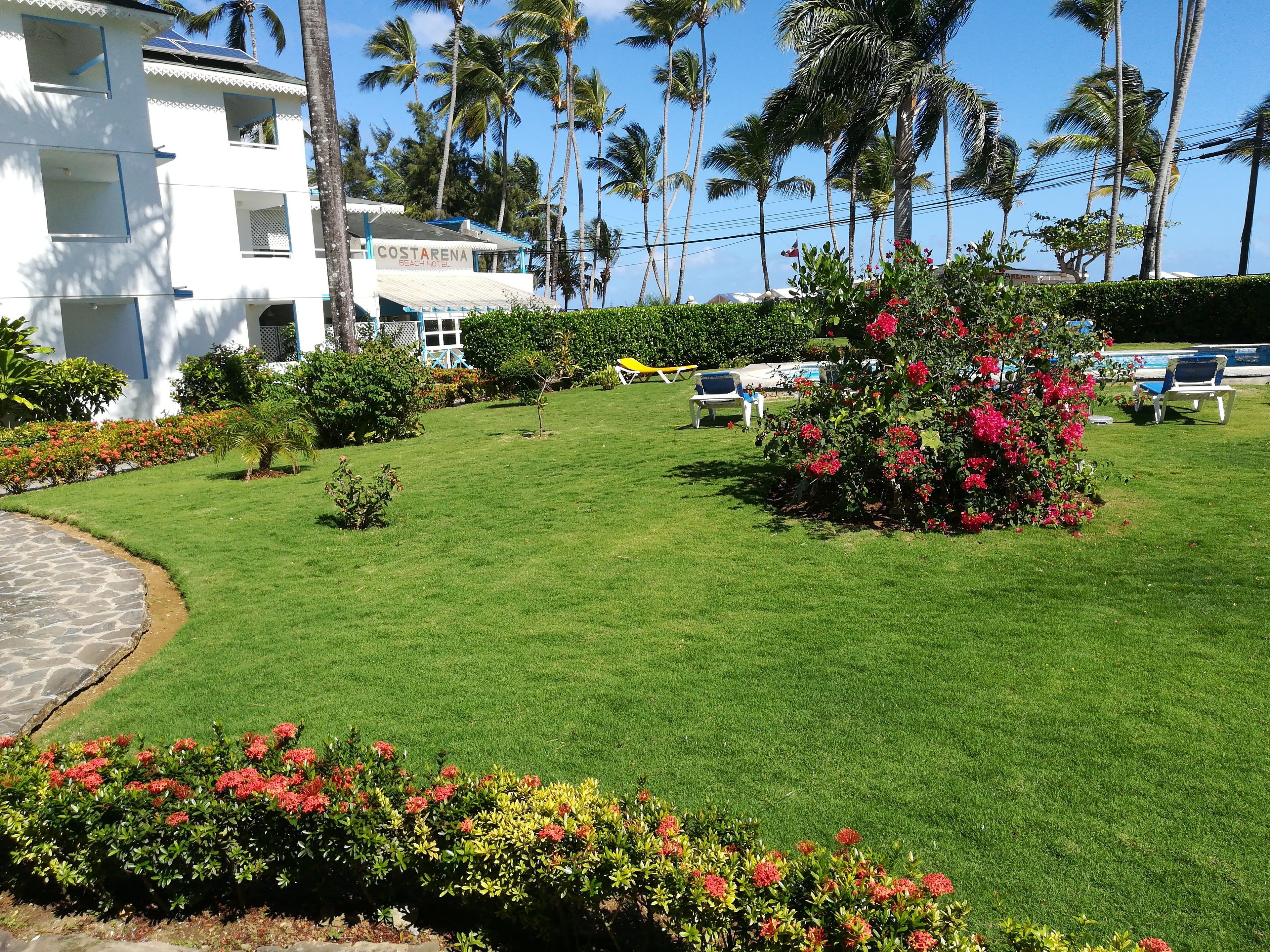 A well-maintained lawn with a pool area, palm trees, and a building labeled "COSTA RENA BEACH HOTEL".