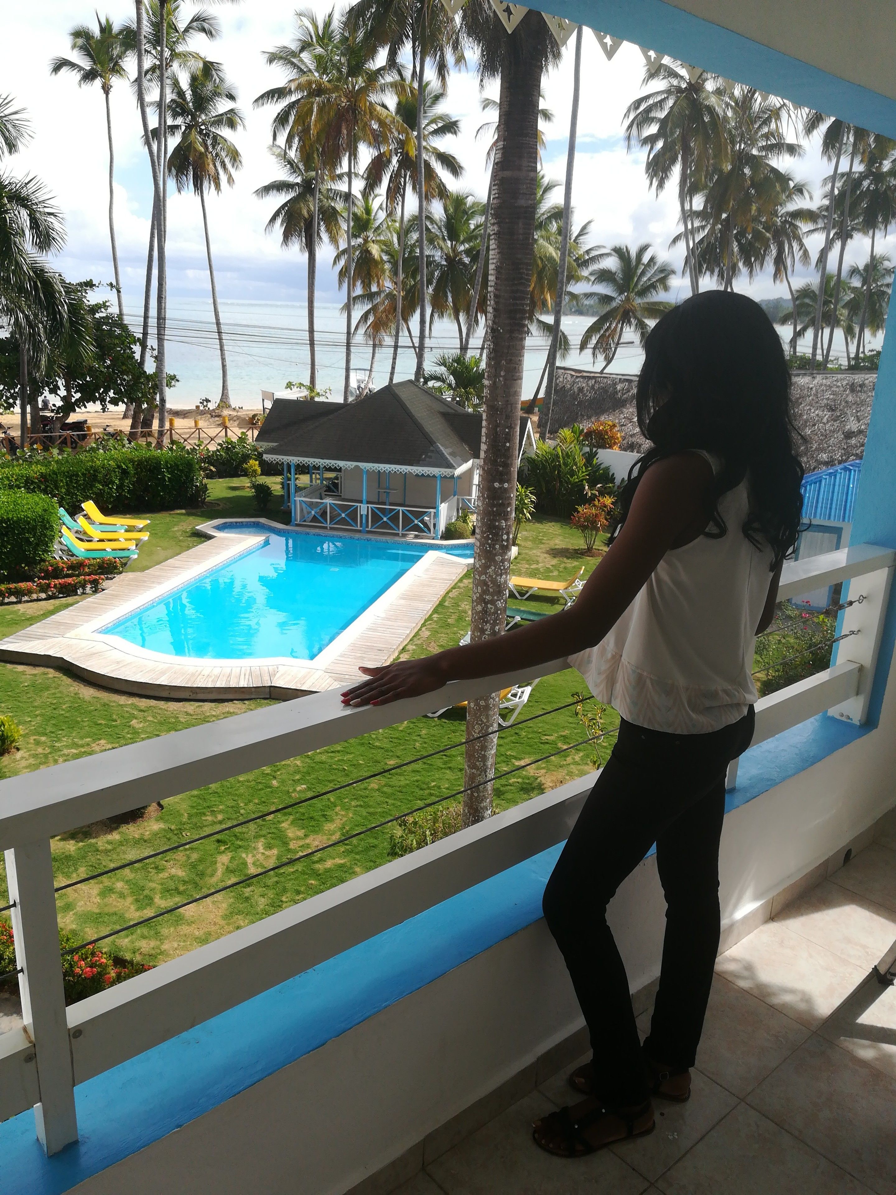 A balcony with a view of a swimming pool, palm trees, and a beach.