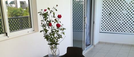 A patio area with a table and chairs, a vase with flowers, and a view of a building through a window.
