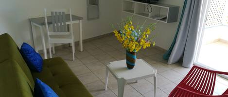 A living room with a green sofa, a white table, a red chair, and a vase of yellow flowers.