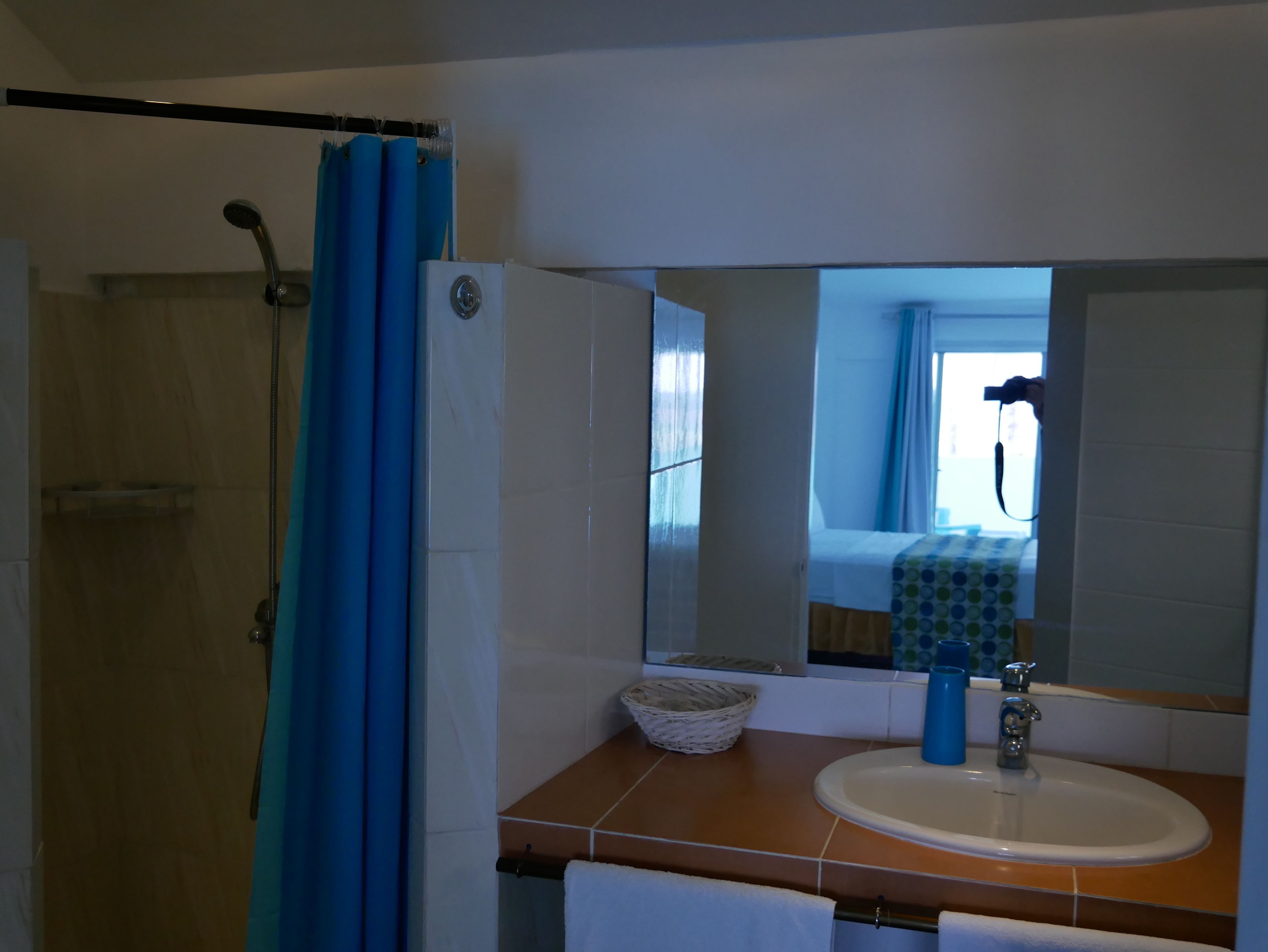 Une salle de bain avec une douche, un lavabo, un miroir et une fenêtre avec des rideaux.