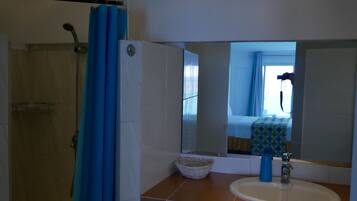 Une salle de bain avec une douche, un lavabo, un miroir et une fenêtre avec des rideaux.