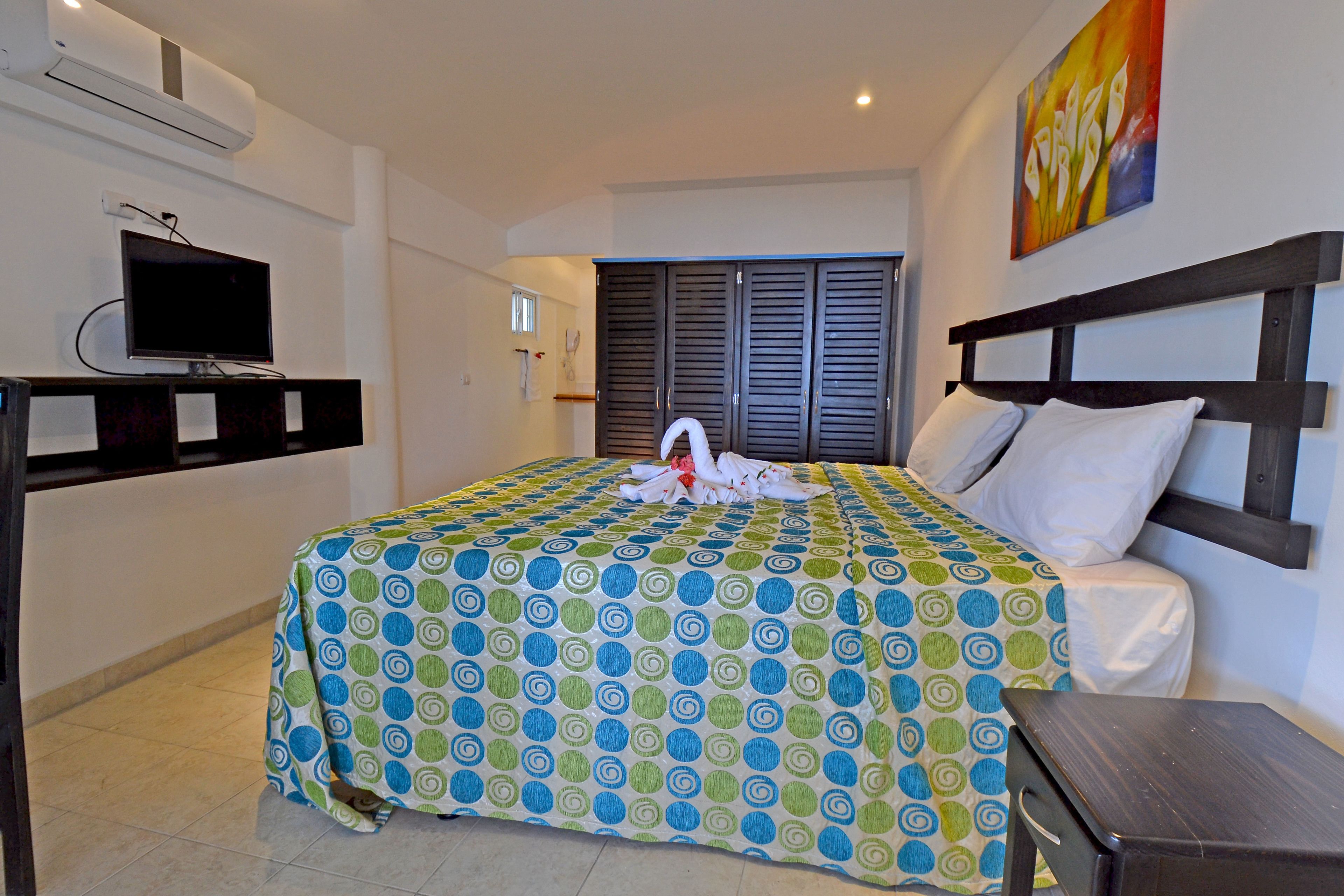A hotel room with a bed, a TV, a wardrobe, and a painting on the wall.
