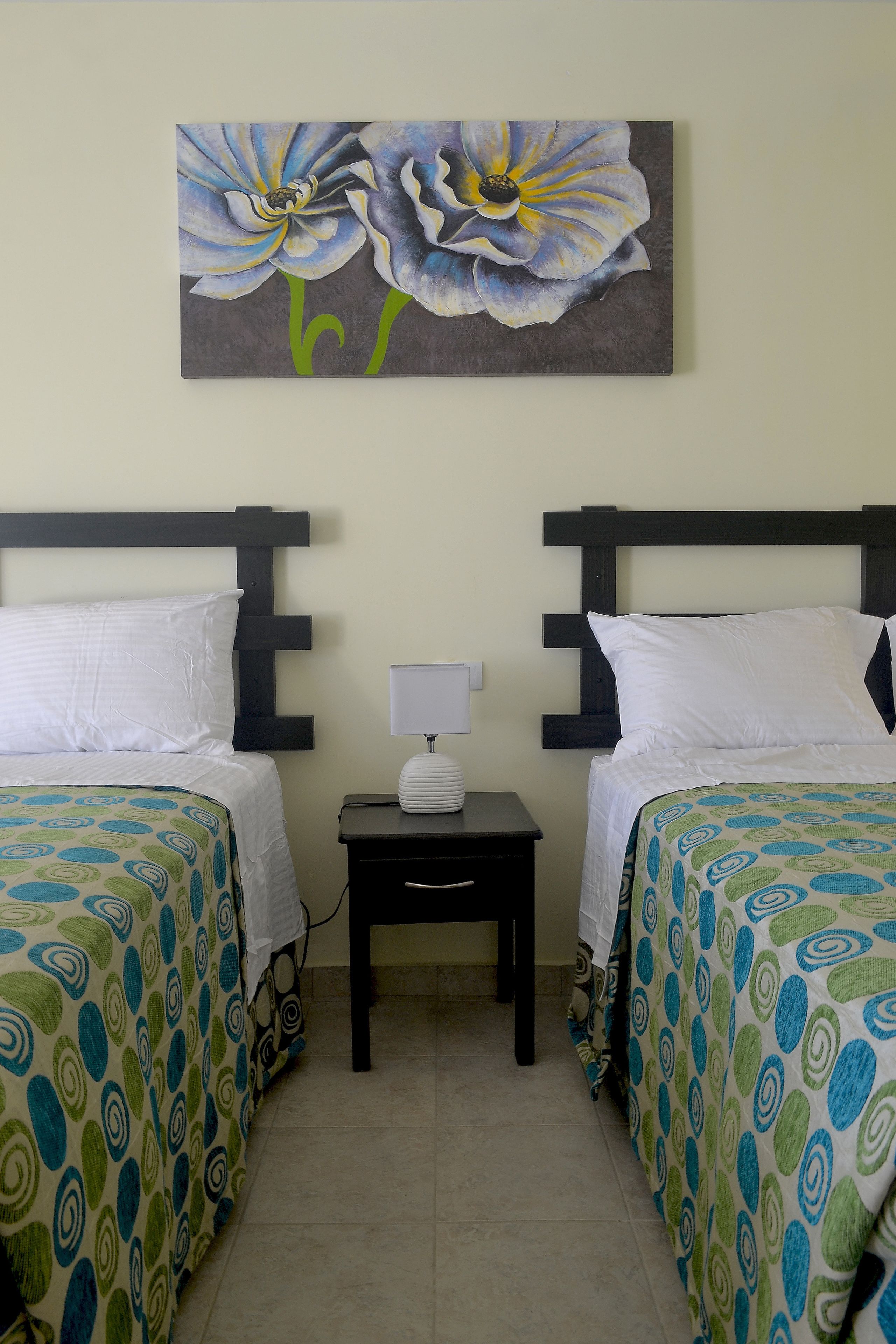 A hotel room with two beds, a nightstand with a lamp, and a painting of flowers on the wall.