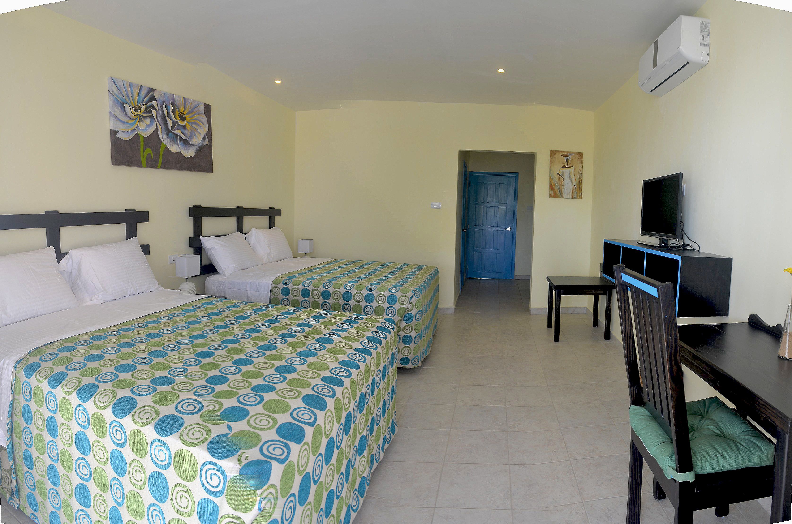 Une chambre d’hôtel avec deux lits, un bureau avec une télévision et une porte donnant sur une autre chambre.