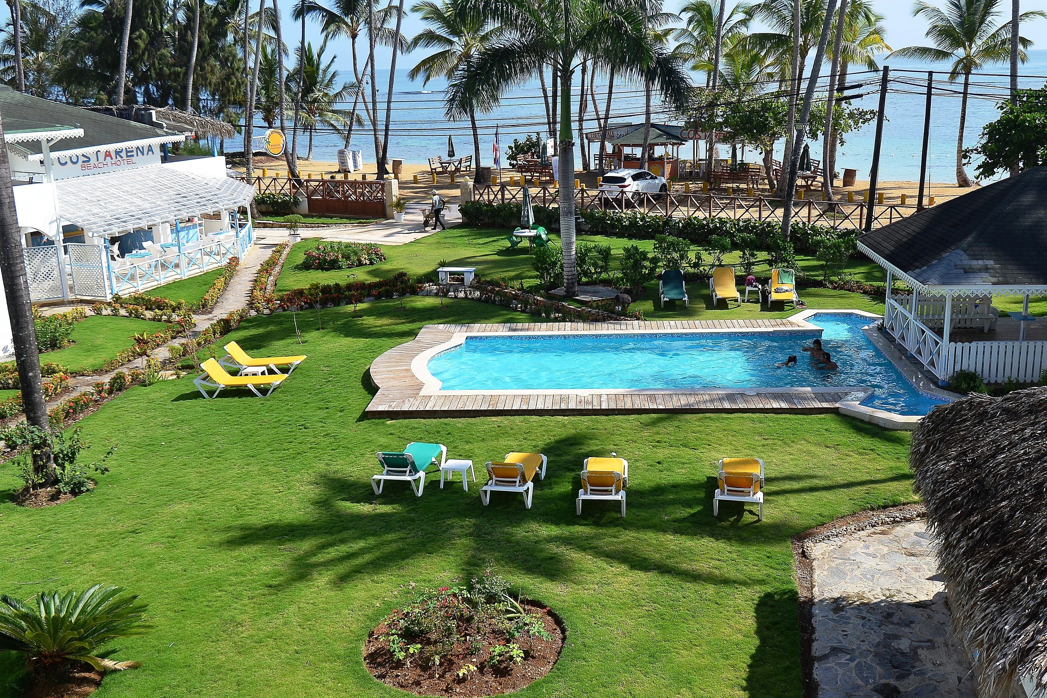 Un espace piscine offrant une vue dégagée sur l’océan, entouré de palmiers et bordé d’une plage.