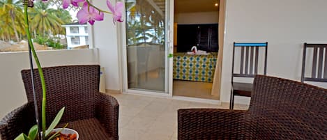 A balcony with wicker furniture, a potted orchid, and a view of a building with palm trees.