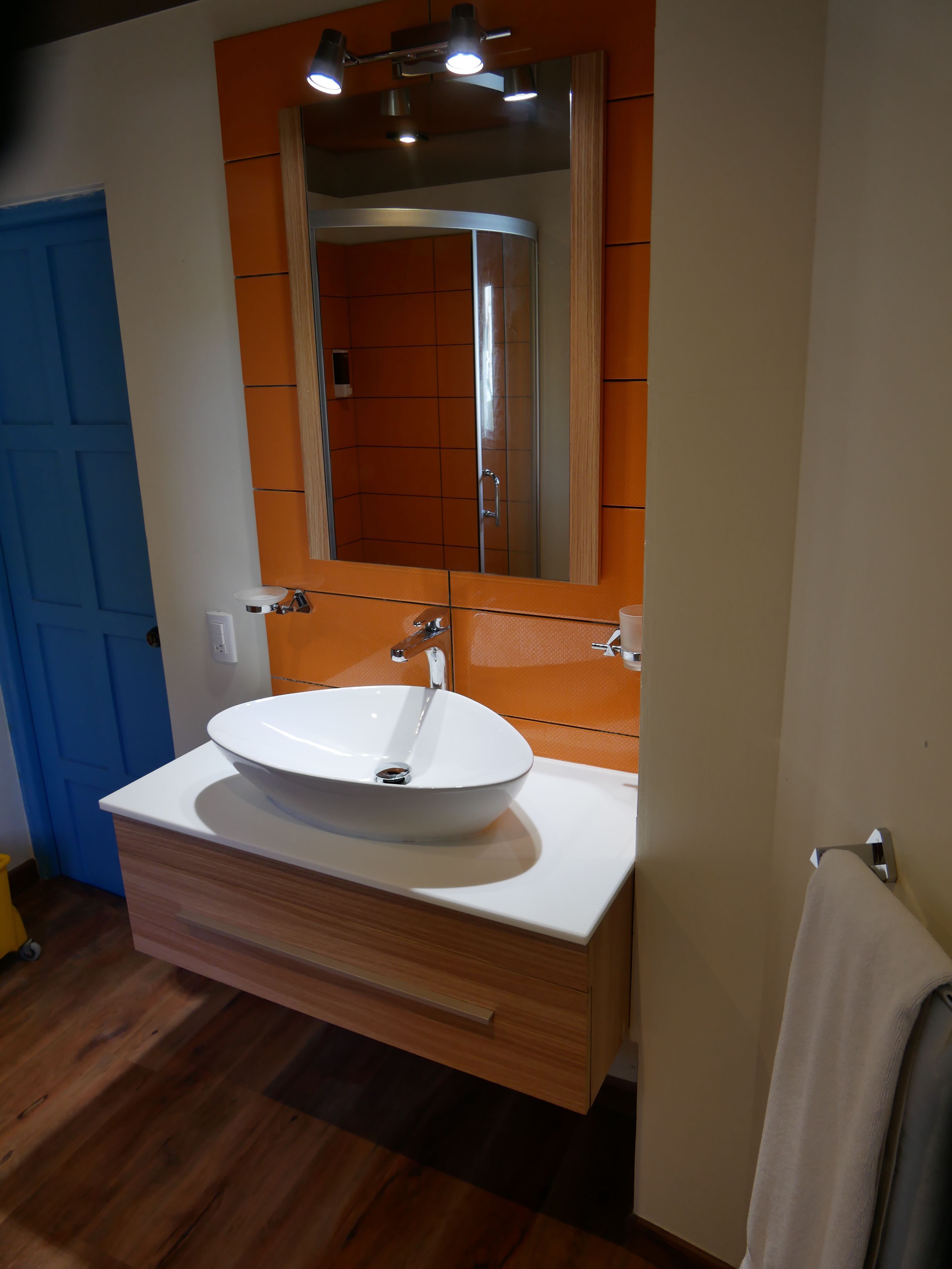 A bathroom with a white sink, wooden vanity, and a mirror with an orange-tiled backsplash.
